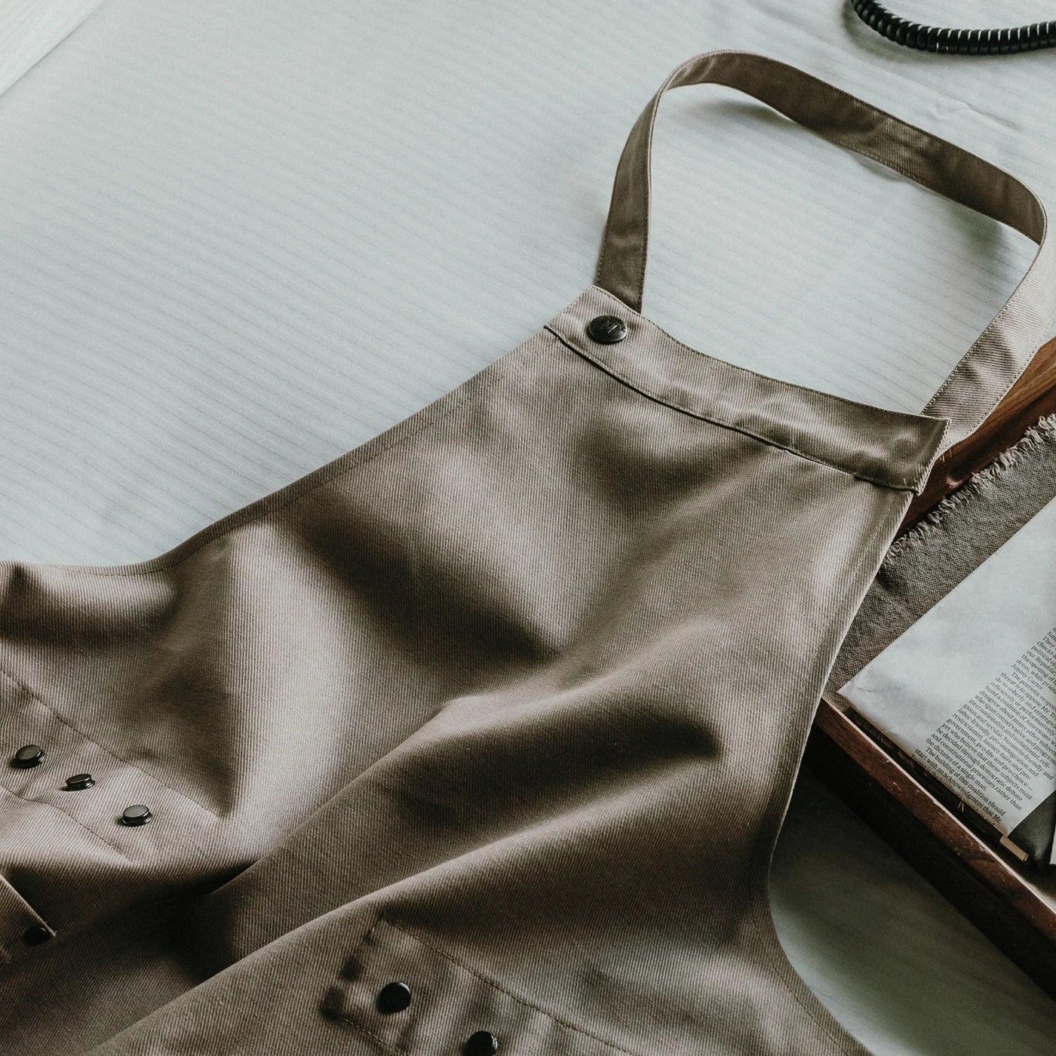 Brown apron on a table with a notebook and pen in the background